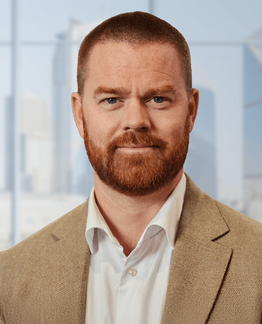 Portrait of Rickard Vikström in a beige blazer and white shirt, standing in an office setting.