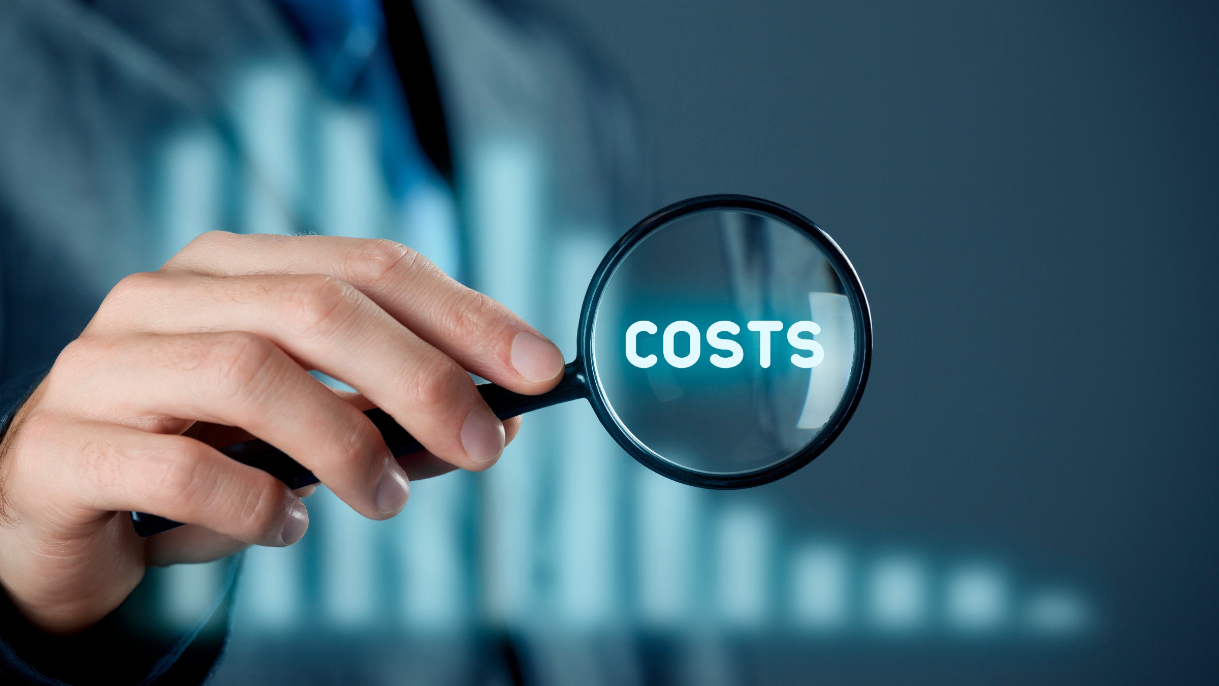 <br />
Close‑up of a person in business attire holding a magnifying glass with the word “COSTS” visible through the lens against a blurred financial‑style background.