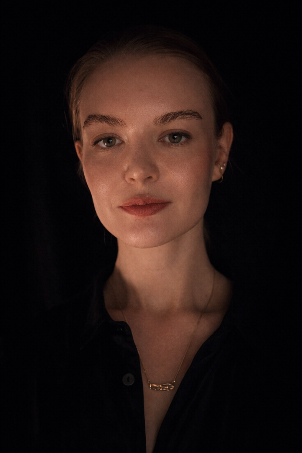 Portrait of Yana Makarochkina against a dark background, wearing a black shirt and a gold necklace.